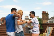 Three male friends carrying ice bucket with bottled beer at rooftop party — Stock Photo