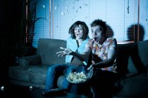 Young couple watching tv, man throwing popcorn — Stock Photo