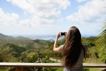 Vista trasera de la mujer tomando fotos del paisaje de la costa - foto de stock