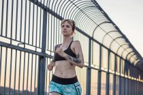 Young tattooed woman running on bridge with sunset behind — Stock Photo