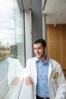 Retrato de jovem médico do sexo masculino sorrindo e de pé na janela — Fotografia de Stock