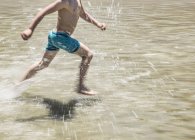 Baixa seção de menino correndo através de águas rasas — Fotografia de Stock
