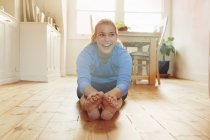 Young woman sitting on floor leaning forwards touching toes — Stock Photo