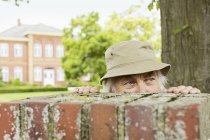 Старший мужчина в шляпе, смотрящий через стену сада — стоковое фото