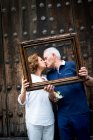Portrait of senior couple, kissing, holding wooden frame in front of their faces, Mexico City, Mexico — Stock Photo