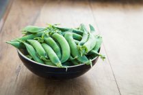 Bowl of green peas on wooden table — Stock Photo