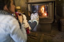 Mujer joven calentando los pies delante del fuego - foto de stock