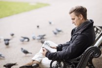 Young man sitting on park bench reading newspaper — Stock Photo