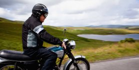 Старший чоловік їде на мотоциклі через сільський пейзаж — стокове фото