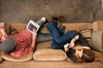 Пара сидящих на диване с помощью цифрового планшета и смартфона — стоковое фото