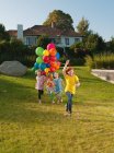 Ragazze che corrono attraverso il prato con palloncini multicolori — Foto stock