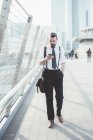 Бизнесмен читает обновление текста смартфона во время прогулки по пешеходному мосту — стоковое фото