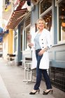 Mature woman in white coat and jeans walking on the street — Stock Photo