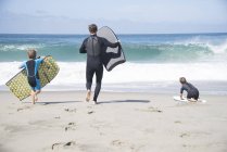 Vista trasera del padre y dos hijos corriendo con bodyboards en la playa, Laguna Beach, California, EE.UU. - foto de stock