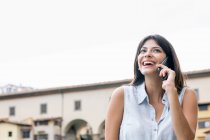 Низкий угол зрения молодой женщины, говорящей по мобильному телефону и улыбающейся, Флоренция, Тоскана, Италия — стоковое фото