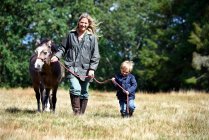Mutter und Sohn gehen Pony auf Feld — Stockfoto