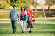 Молодая пара и дочь с кучей красных воздушных шаров прогуливаются в парке — стоковое фото