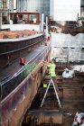 Travailleur sur échelle de marche vérifiant bateau dans l'atelier chantier naval — Photo de stock