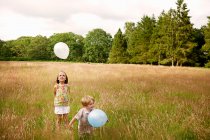 Brother and sister in tall grass playing with balloon — Stock Photo
