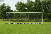 Футбольные ворота на зеленой траве, полной мячей — стоковое фото