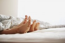 Los pies desnudos de los padres y el hijo acostado en la cama - foto de stock