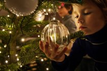 Boy decorating Christmas tree with baubles at home — Stock Photo