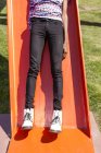 Pernas e botas brancas de homem jovem em slide playground laranja — Fotografia de Stock