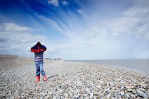 Boy on pebble beach with coat over his head — Stock Photo