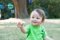 Portrait of cute baby boy reaching for bubbles in park — Stock Photo