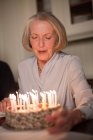 Senior woman blowing out candles on birthday cake — Stock Photo