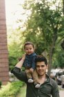 Baby boy sitting on fathers shoulder, looking at camera smiling — Stock Photo