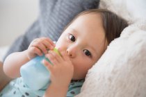 Portrait of baby boy on sofa drinking from baby cup — Stock Photo