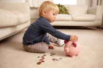 Junge steckt Münzen in Sparschwein — Stockfoto