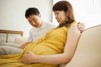 Man looking at pregnant woman's stomach on sofa — Stock Photo