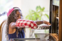 Mädchen mit Ofenhandschuh schiebt Kuchenformen in den Ofen — Stockfoto