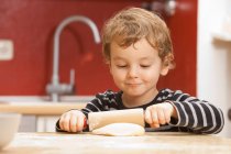 Мальчик катит тесто на кухне — стоковое фото