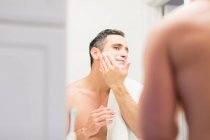 Hombre adulto medio, mirando en el espejo, aplicando espuma de afeitar a la cara, vista trasera - foto de stock