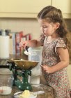 Girl weighing ingredients in kitchen — Stock Photo