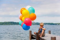 Boy holding balloons on wooden pier — Stock Photo
