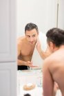 Homem adulto médio, olhando no espelho, aplicando espuma de barbear no rosto, visão traseira — Fotografia de Stock