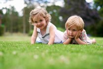 Nivel de superficie del niño y la niña acostados en la hierba - foto de stock