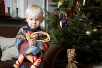 Menino segurando brinquedo pela árvore de Natal — Fotografia de Stock