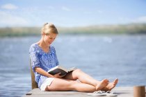 Жінка читає книгу на березі озера — стокове фото