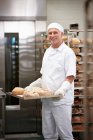 Шеф-повар несет поднос с хлебом на кухне — стоковое фото