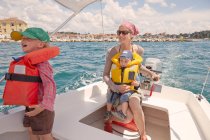 Зрелая женщина с двумя мальчиками за рулем моторной лодки, Ровинь, полуостров Истрия, Хорватия — стоковое фото