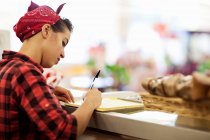 Young woman writing on counter of bakery — Stock Photo