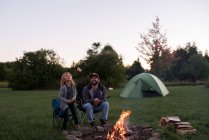 Père et fille assis à côté du feu de camp, rôtissant des guimauves sur le feu — Photo de stock