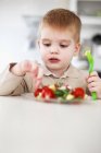 Boy picking at plate of fruit in kitchen — Stock Photo