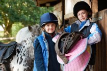 Two girls holding saddles with pony — Stock Photo