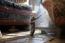 Worker cleaning boat with high pressure hose in shipyard — Stock Photo